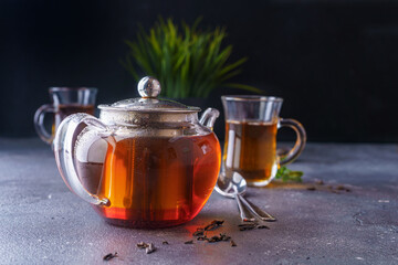 Black tea in a clear glass teapot on a dark background. 