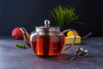 Black tea in a clear glass teapot on a dark background. There's a cake in the back