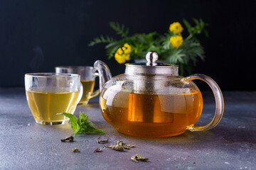 Green tea in a clear glass teapot on a dark background