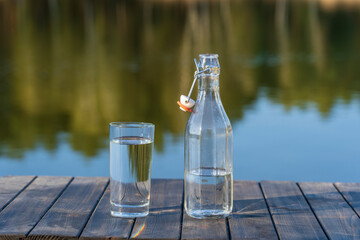 Glass and bottle with drinking water on a wooden table in the morning near the lake. Nature and travel concept