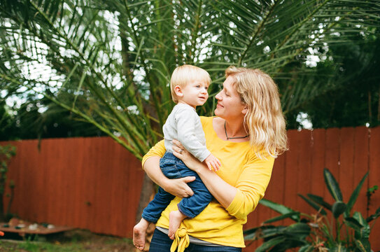 Blond mid-30's mom holding young son in backyard
