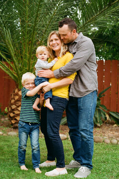 Happy parents with 2 young sons in backyard group hug 