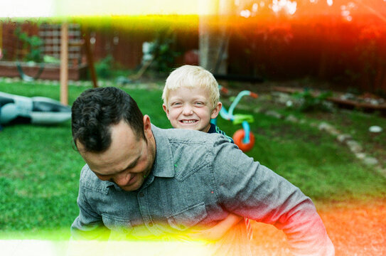 Young son riding on dad's back while playing in backyard