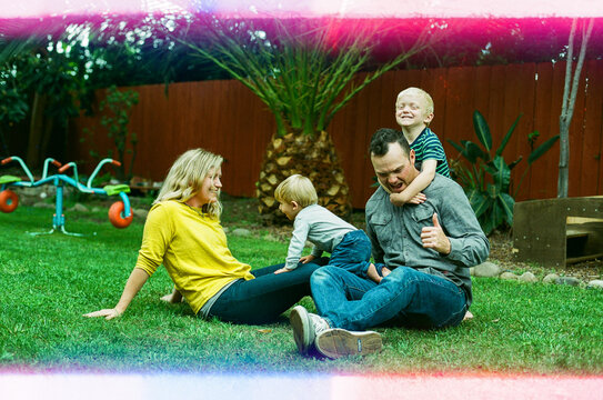 Mom and dad playing with two young boys in the grass in backyard