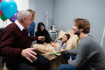 A family surrounding a little girls bed, she is staying in a hospital after an accident, they came to visit