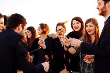 Crop happy colleagues with sparklers during festive event outdoors