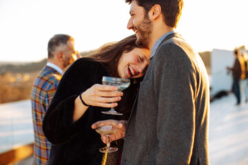 Crop happy colleagues with alcoholic beverages on rooftop in sunlight