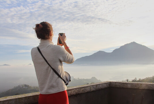 Woman taking photo of volcanoes on phone at sunrise