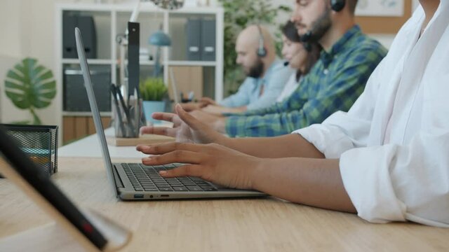 Close-up of female hands typing with laptop while people in background working in call center talking to customers online helping with client support