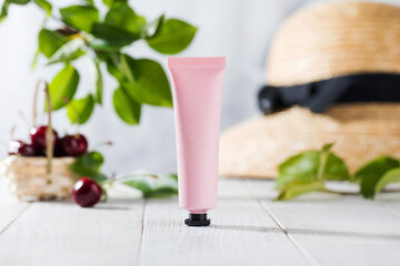 Pink tube of cosmetics, cream for the skin on a summer background with cherry berries and leaves. Natural cosmetics.