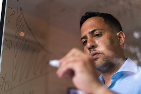 Latin hispanic man working at home and writting graphs on glass wall