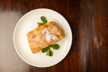 Slice of delicious fresh baked Rustic Apple Pie served on a white plate on wooden table background.