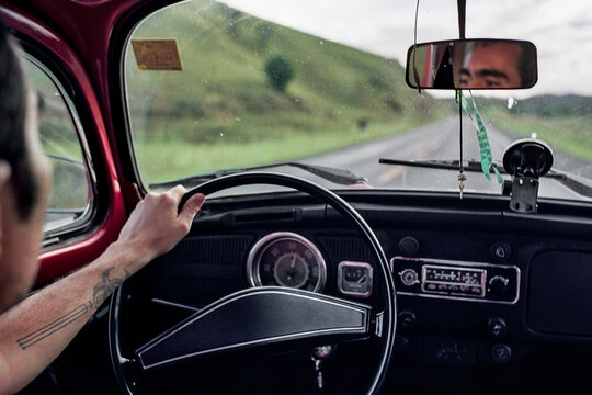 Point of view of a man driving a red vintage car in the mountains
