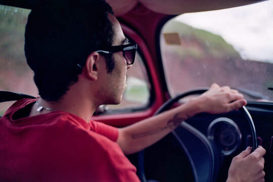 Man wearing a red t-shirt and sun glaces drives a red vintage car in the mountains