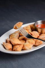 Fried dumplings stuffed with meat and served with tomato sauce on a white plate.