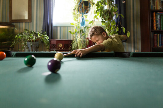 Boy squints down pool cue
