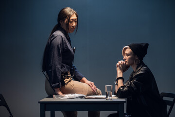 A female investigator sits on a table and interrogates a young criminal in an interrogation room