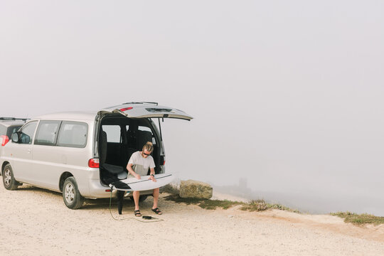 Bearded Man Waxing Surfboard On the back of Car
