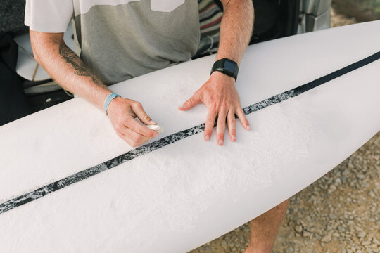 Closeup of hands waxing surfboard

