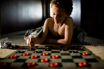 Smiling boy plays checkers on floor