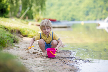 Little toddler child, cute boy, playing with toys in the sand on a lake
