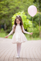 Fototapeta na wymiar Happy girl in holiday dress with pink ballon walking in city park, enjoying the life. Family outdoor lifestyle. Celebration concept. Cute little school girl in green summer park