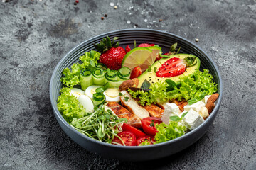 Healthy dinner. Buddha bowl lunch with grilled chicken and avocado, feta cheese, quail eggs, strawberries, nuts and lettuce on gray background. Flat lay. Top view