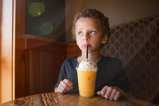 Cute boy drinks mango smoothie at cafe
