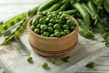 Bowl with pea seeds and fresh pea on wooden background