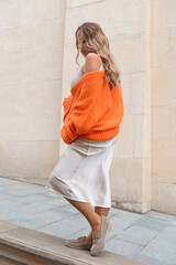 Portrait of fashionable women in orange sweater and beige dress posing in the street