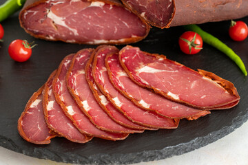 Turkish pastrami on a black stone serving plate. Whole and sliced pastrami. Pastrami is made from the ribeye and beef fillet parts of the cow. close up pastrami or bacon. local name kayseri pastırma