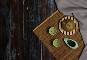 Fototapeta premium Chinese Tea Ceremony. Brown ceramic teapot and turquoise tea cup. Green tea on bamboo mat on aged wooden table. Top view. 