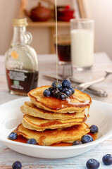 Close-up delicious pancakes, with fresh blueberries and maple syrup on a light background, sweet maple syrup flows from 
