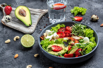 keto diet food. Keto breakfast grilled chicken and avocado, feta cheese, quail eggs, strawberries, nuts and lettuce on gray background