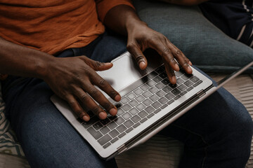 Anonymous black man's hands typing on modern laptop