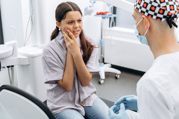 Girl touches her cheeks with her hand. A cute, crooked girl tells the dentist that she has a toothache.