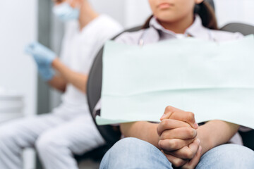 Girl in the dental chair is worried, she clenched her fists. The girl is afraid to treat her teeth