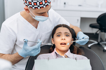 Scared girl in a dental chair, afraid of the injection. The dentist holds a syringe with a needle in his hand.