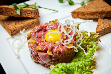 Veal tartar with quail egg and rye toast. Close-up, selective focus