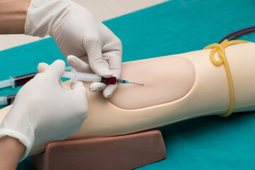 Doctor or nurse hands in medical white gloves using needle syringe drawing blood sample from...