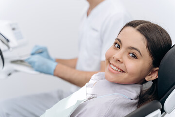 Attractive girl sitting in a dental chair, looking at the camera. Beautiful little girl smiling