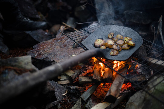 Potatoes being cooked over an open fire in a shovel