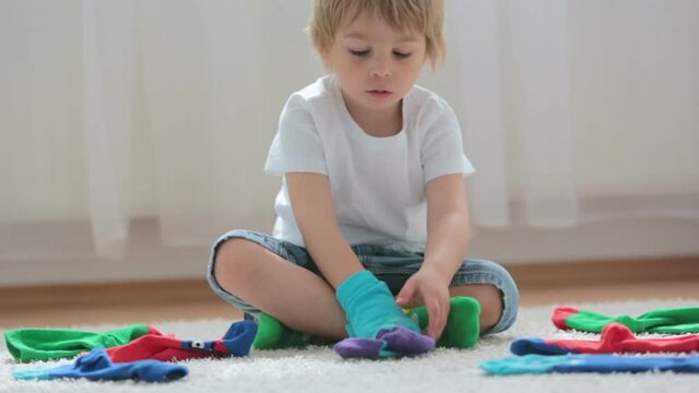 Child, toddler boy, pairing different colorful socks, sitting on the floor