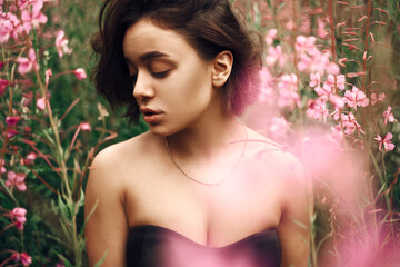 Naklejka premium Beautiful brown-haired girl in a black top outdoors In a meadow with pink flowers