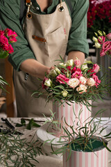 Florist make gift bouquets in hat boxes. Graceful female hands make a beautiful bouquet. Florist workplace. Small business concept. Front view. Flowers and accessories. Vertical shot