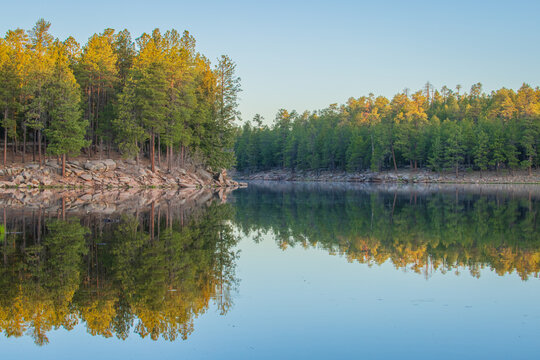 reflections on a cool mountain lake surrounded by Pine trees and orange shaded rocks has a sense of natural calmness only found by the still waters of a forested lake