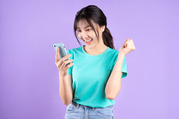 Young asian girl in cyan shirt using phone on purple background - Powered by Adobe
