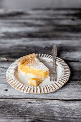 Slice of lemon pie on white ceramic plate, grey wooden background, selective focus, copy space