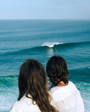 Two girls look at the ocean from a high hill