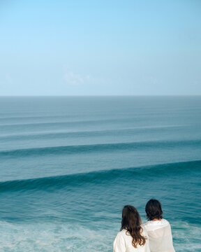 Two girls look at the ocean from a high hill